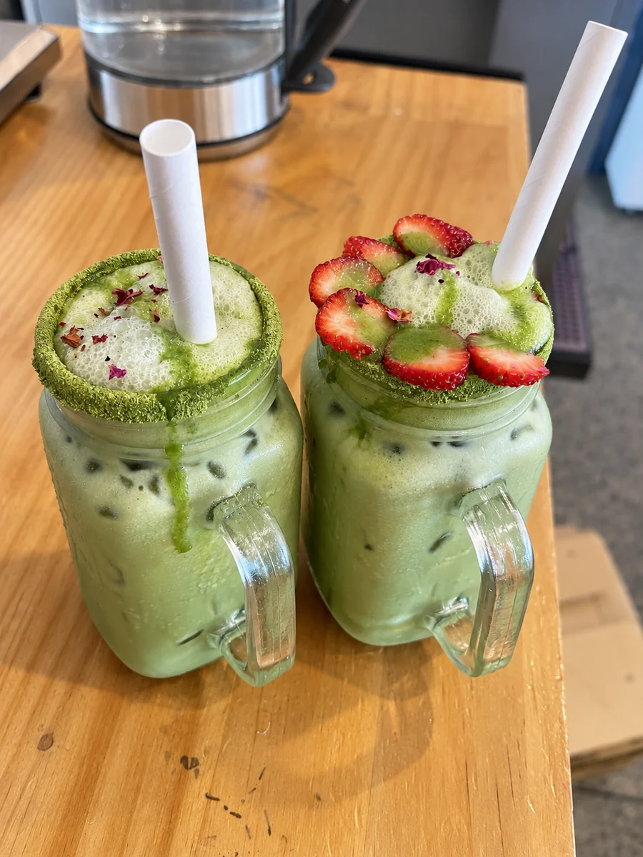Two iced matcha drinks topped with strawberries and kiwi